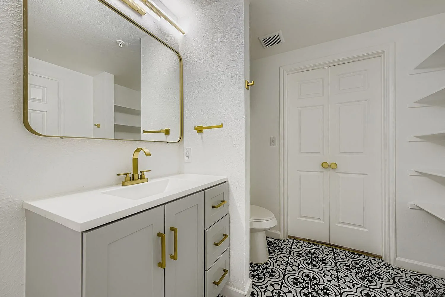 Primary bathroom, white vanity with brass hardware, patterned tile flooring, rounded mirror