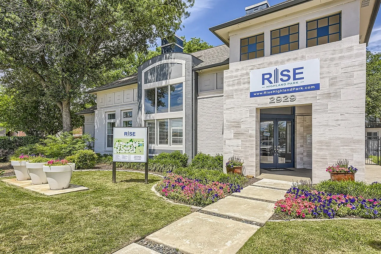 Modern white brick building with curved glass entryway, landscaped front with flowering plants, Dallas TX