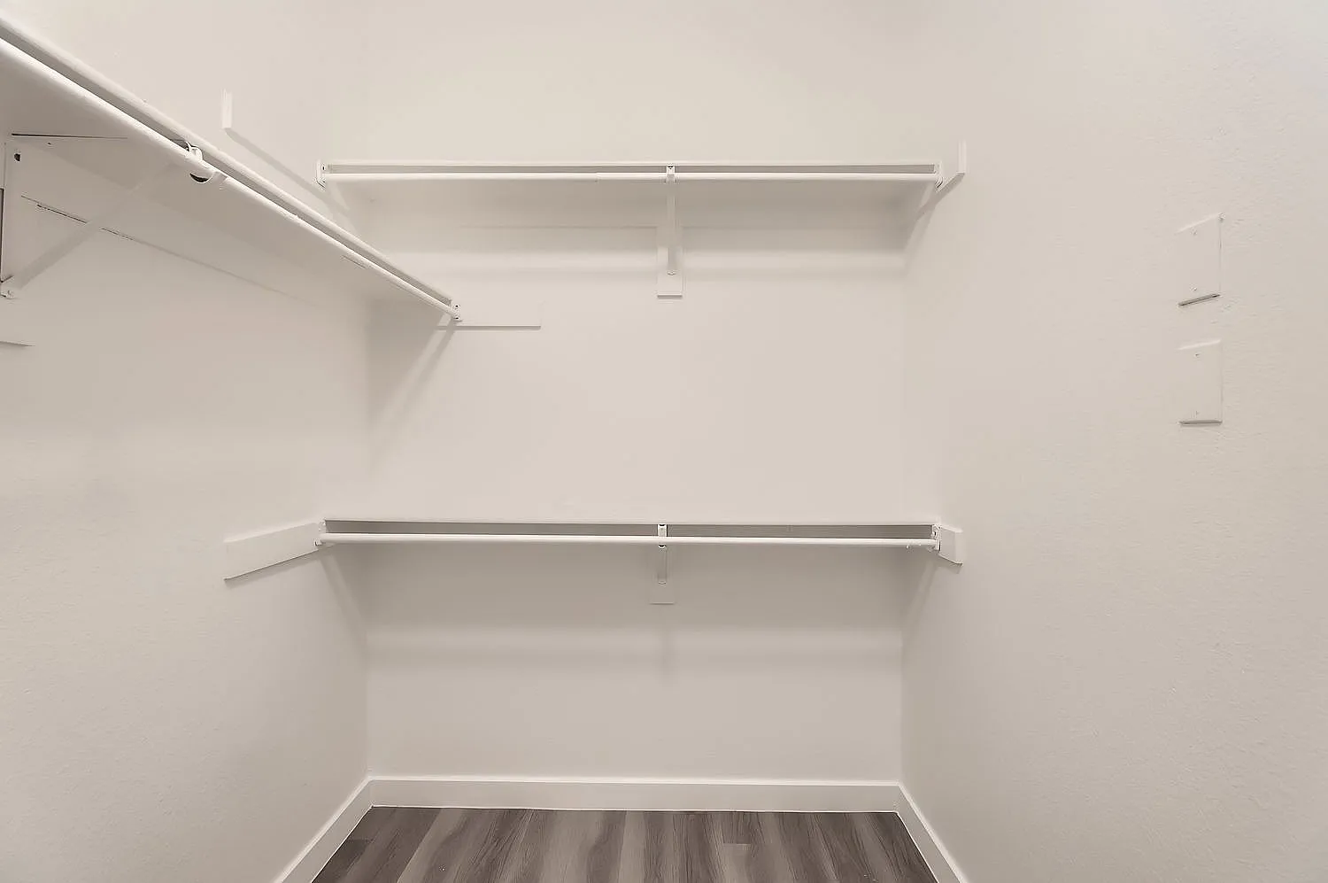 Walk-in closet, white shelves, white walls, wood-style plank flooring
