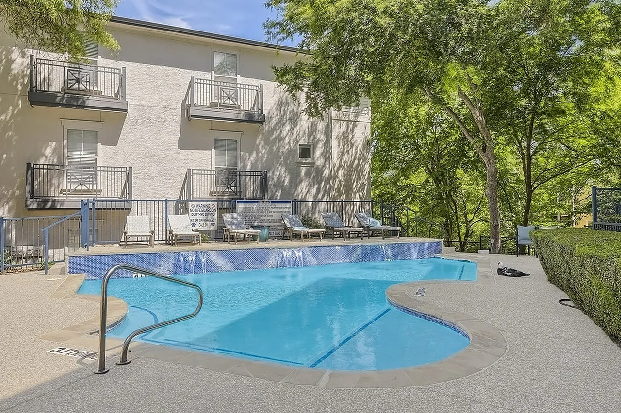 Resort-style swimming pool, concrete deck, metal handrail, building with white siding