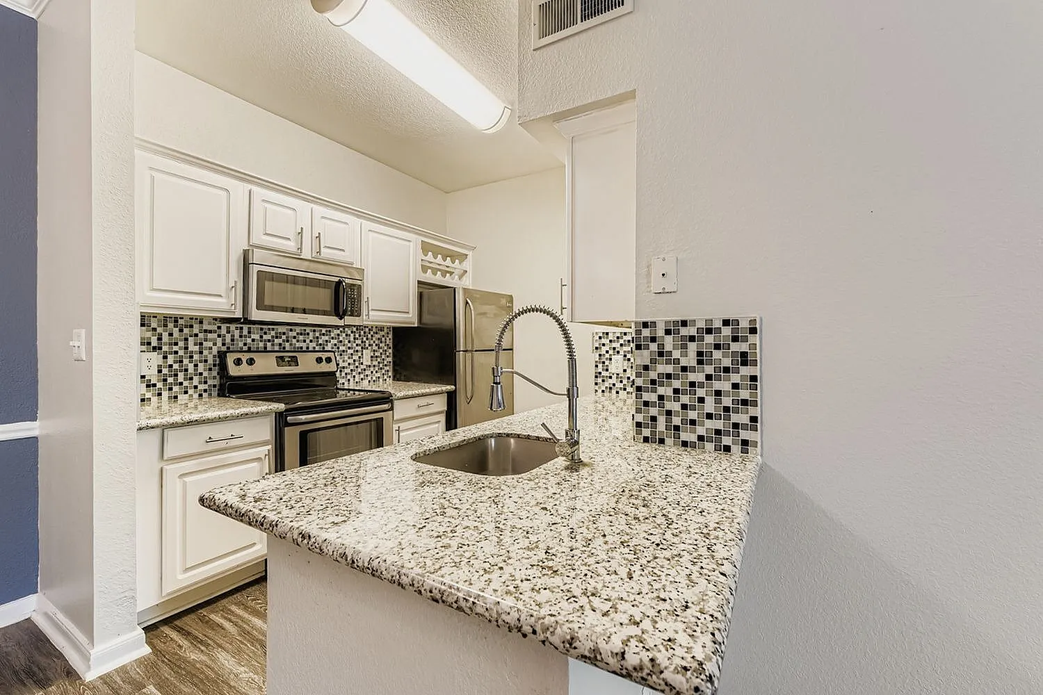 Kitchen, white shaker cabinetry, speckled granite countertops, stainless steel appliances, mosaic tile backsplash, wood-style plank flooring