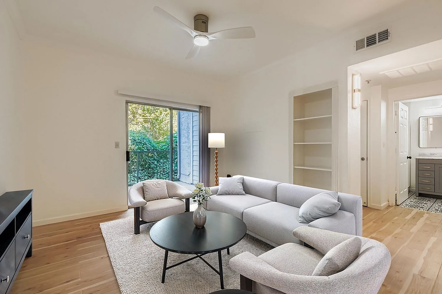 Living room, curved gray sofa, wood-style plank flooring, ceiling fan, glass patio door