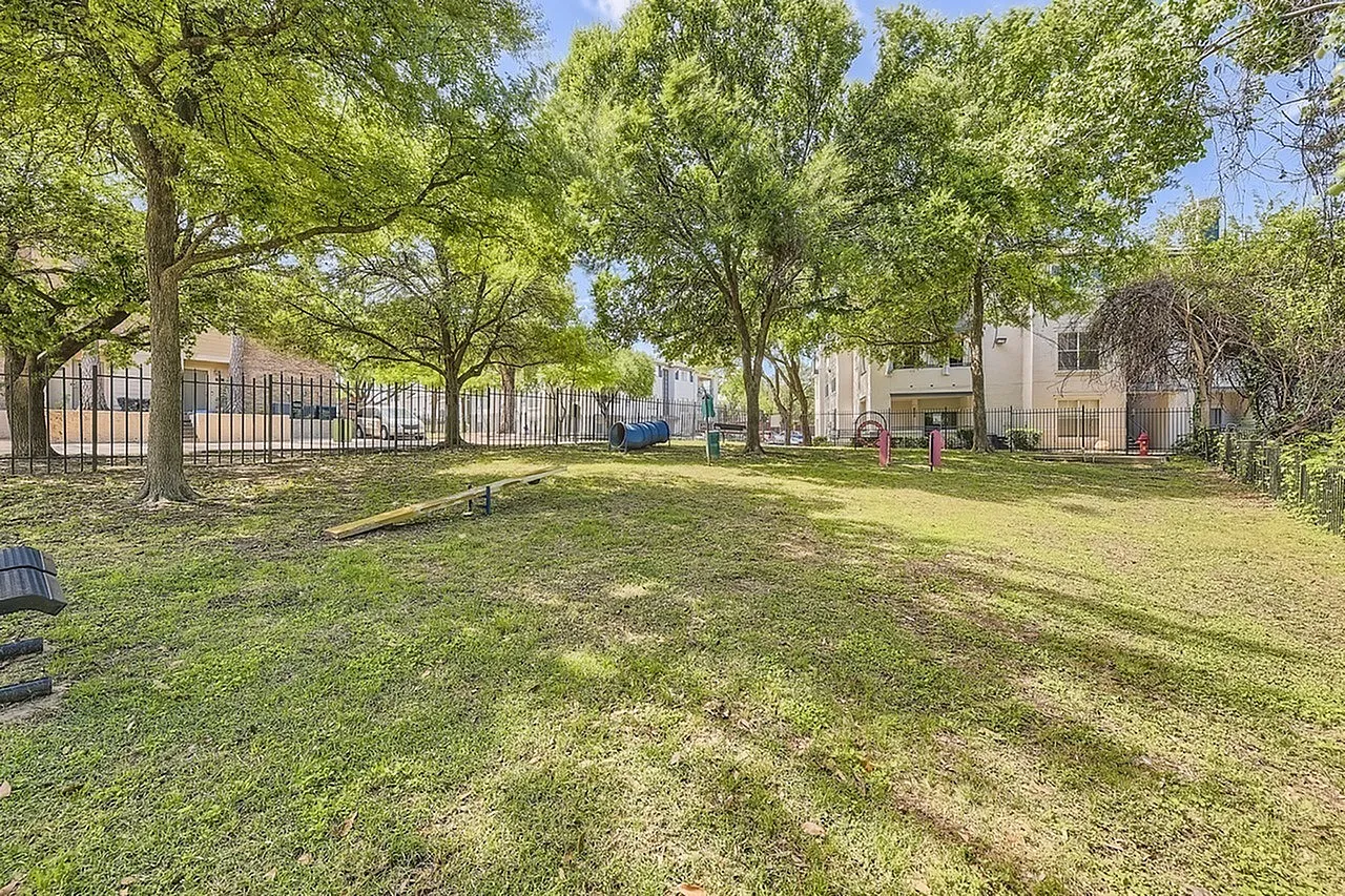 Courtyard with large mature trees, green lawn, metal fence, residential buildings