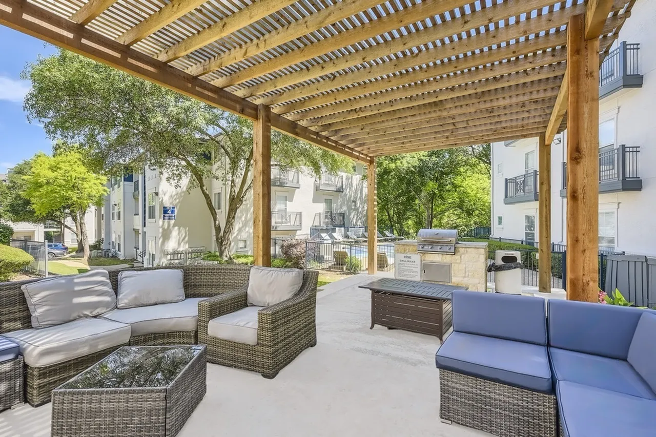 Covered patio, woven wicker seating, blue cushions, wood pergola roof, gas grill