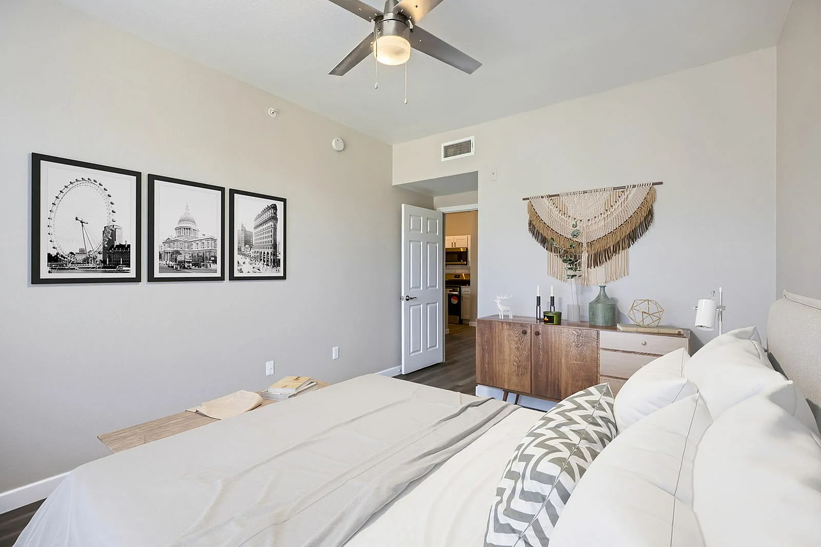 Primary bedroom, wood-style plank flooring, ceiling fan, framed black and white artwork, wood dresser with decorative decor