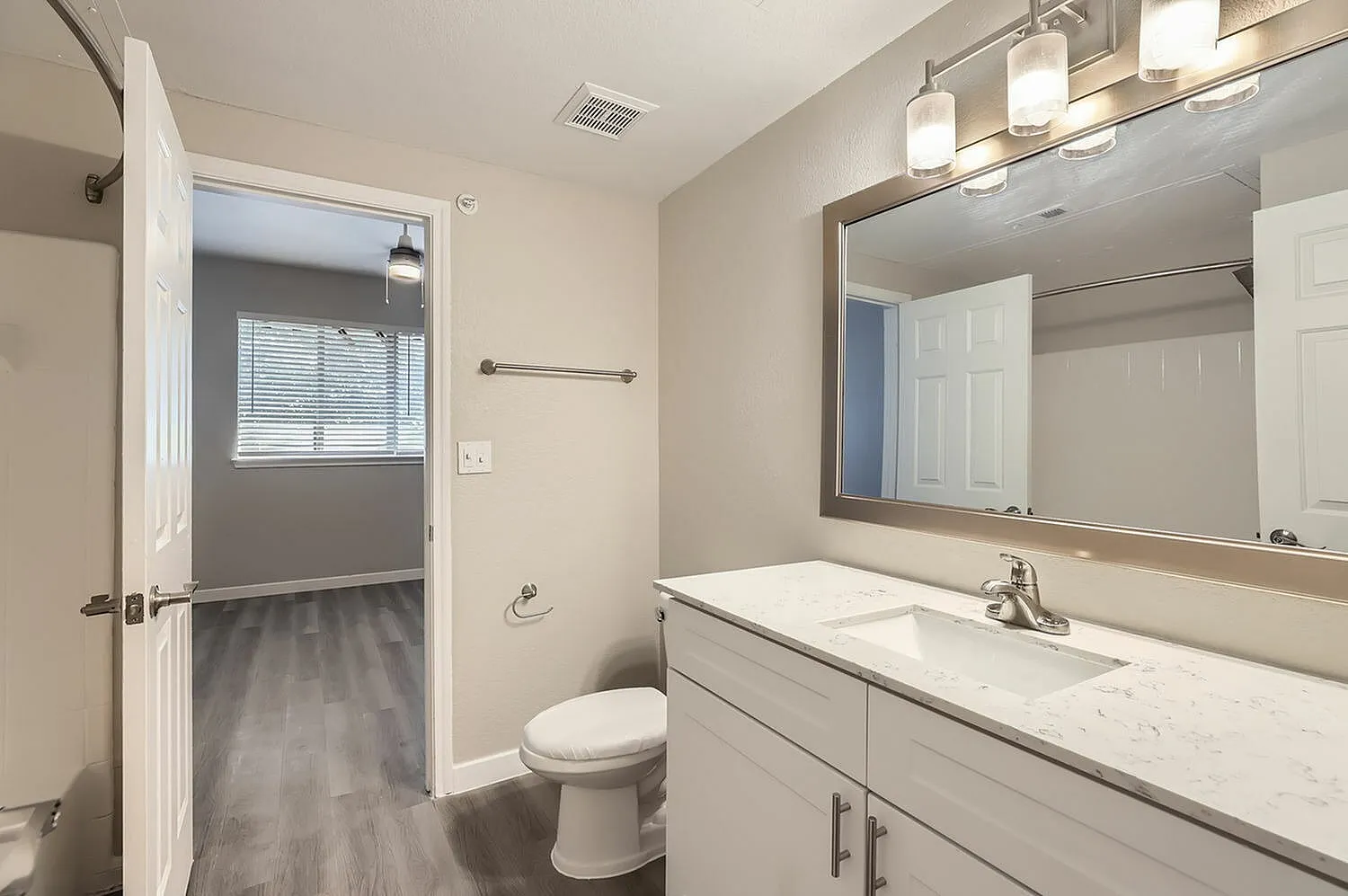 Primary bathroom, white marble countertops, framed mirror, wood-style plank flooring, fixtures and lighting