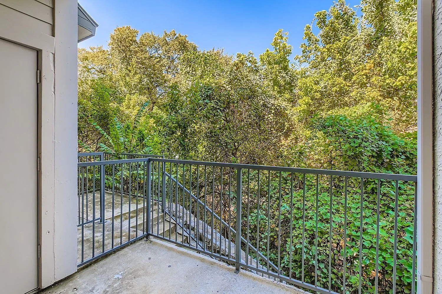 Balcony, metal railing, concrete flooring, lush green trees