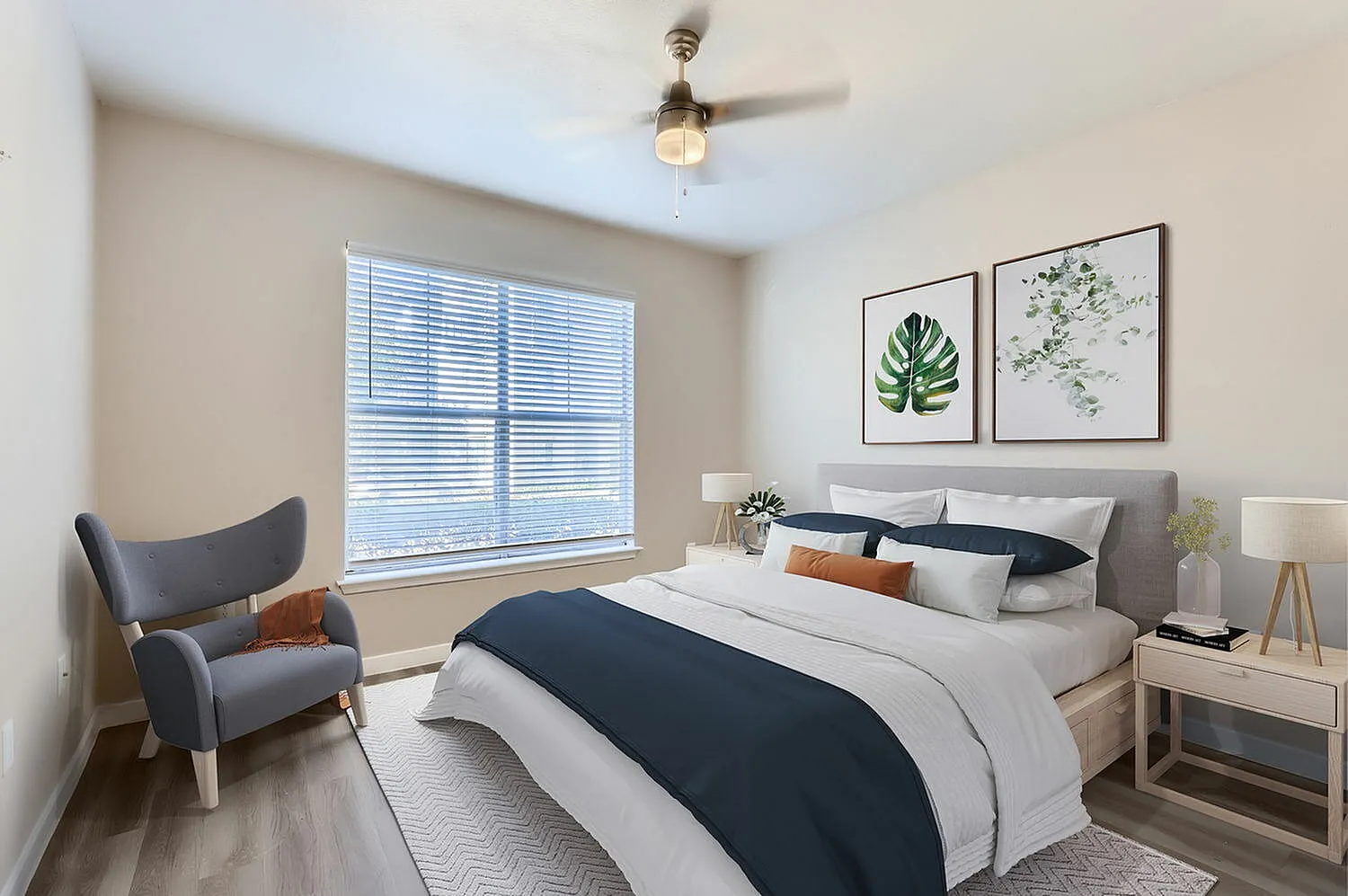 Primary bedroom, gray upholstered headboard, wood-style plank flooring, ceiling fan, botanical artwork