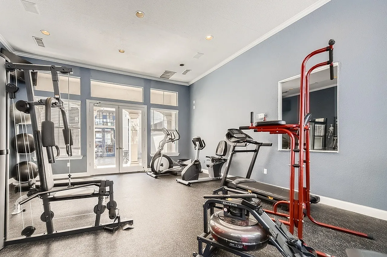 Fitness center with cardio equipment, red leg press machine, wood-style plank flooring