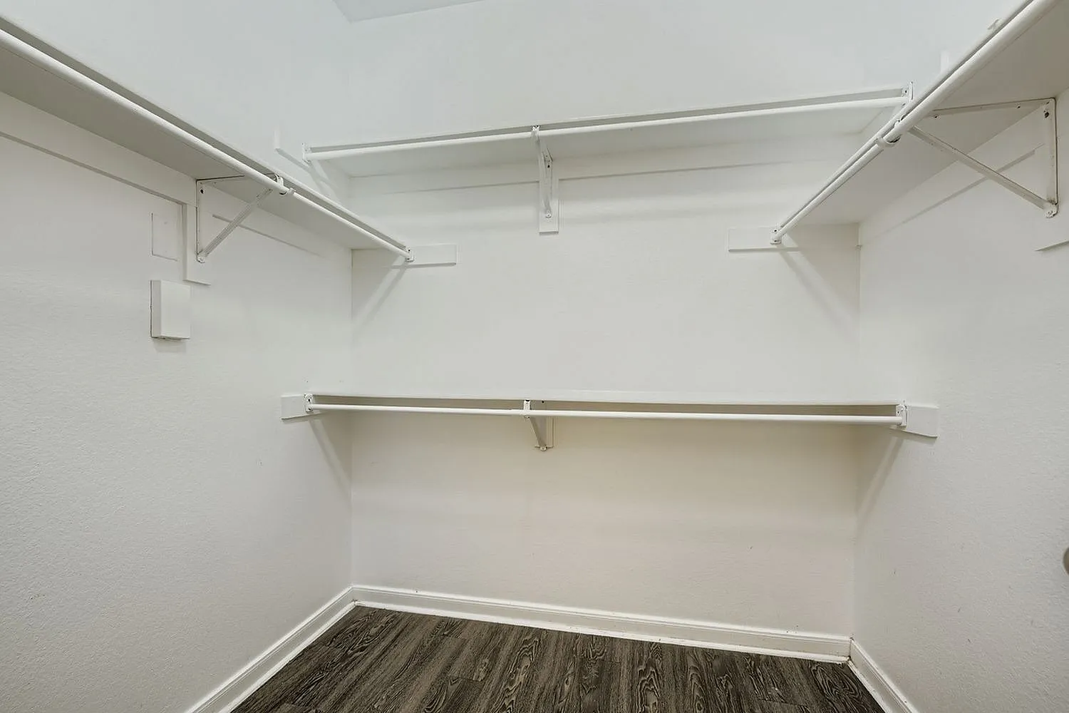 Walk-in closet, white painted walls, metal shelving rods, wood-style plank flooring