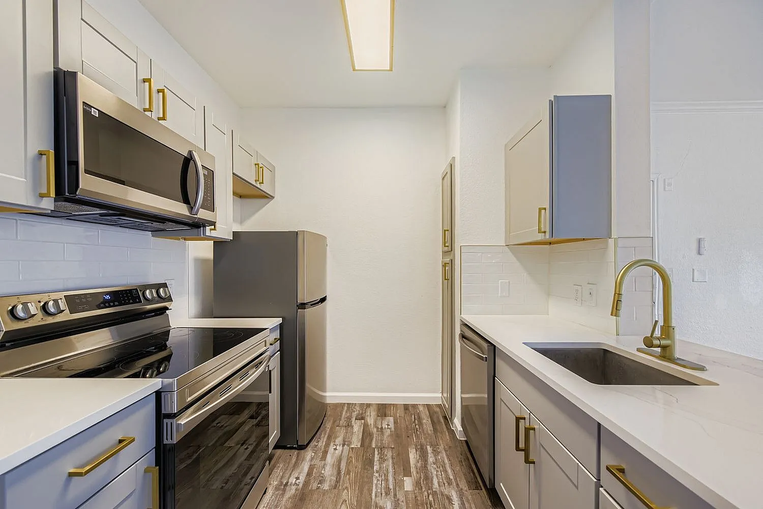 Galley kitchen, wood-style plank flooring, stainless steel appliances, quartz countertops, brass hardware
