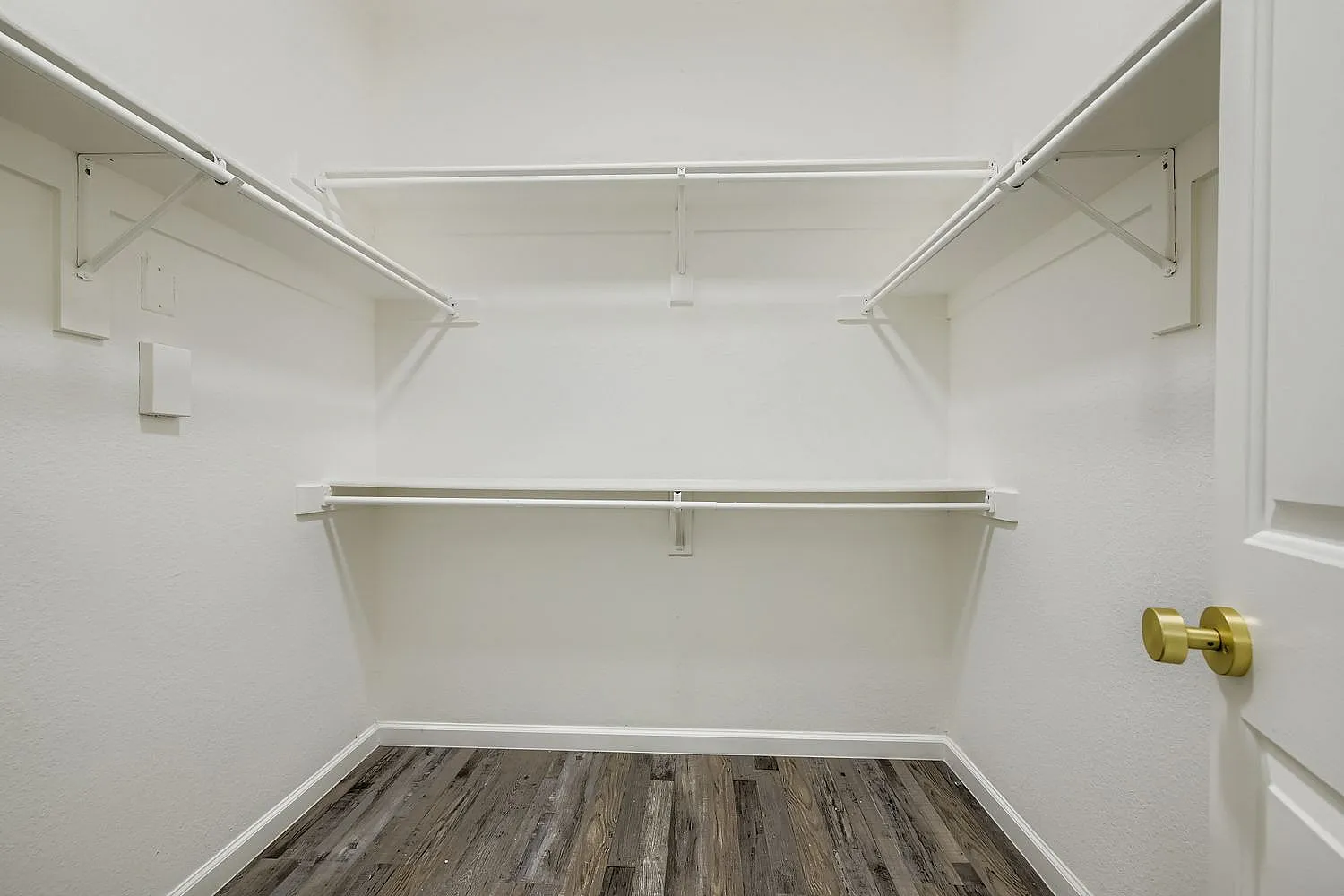 Walk-in closet, wood-style plank flooring, shelving rods, white walls, brass hardware