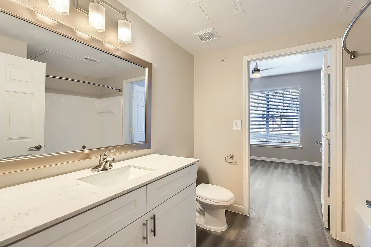 Primary bathroom, white quartz countertop, white cabinetry, framed mirror, wood-style plank flooring