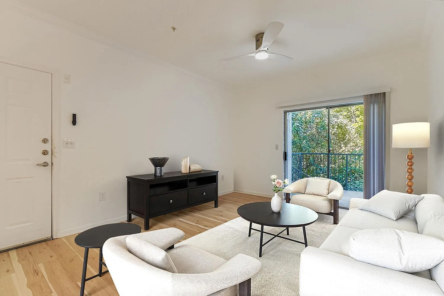 Living room, cream upholstered seating, black round coffee table, wood-style plank flooring, sliding glass doors