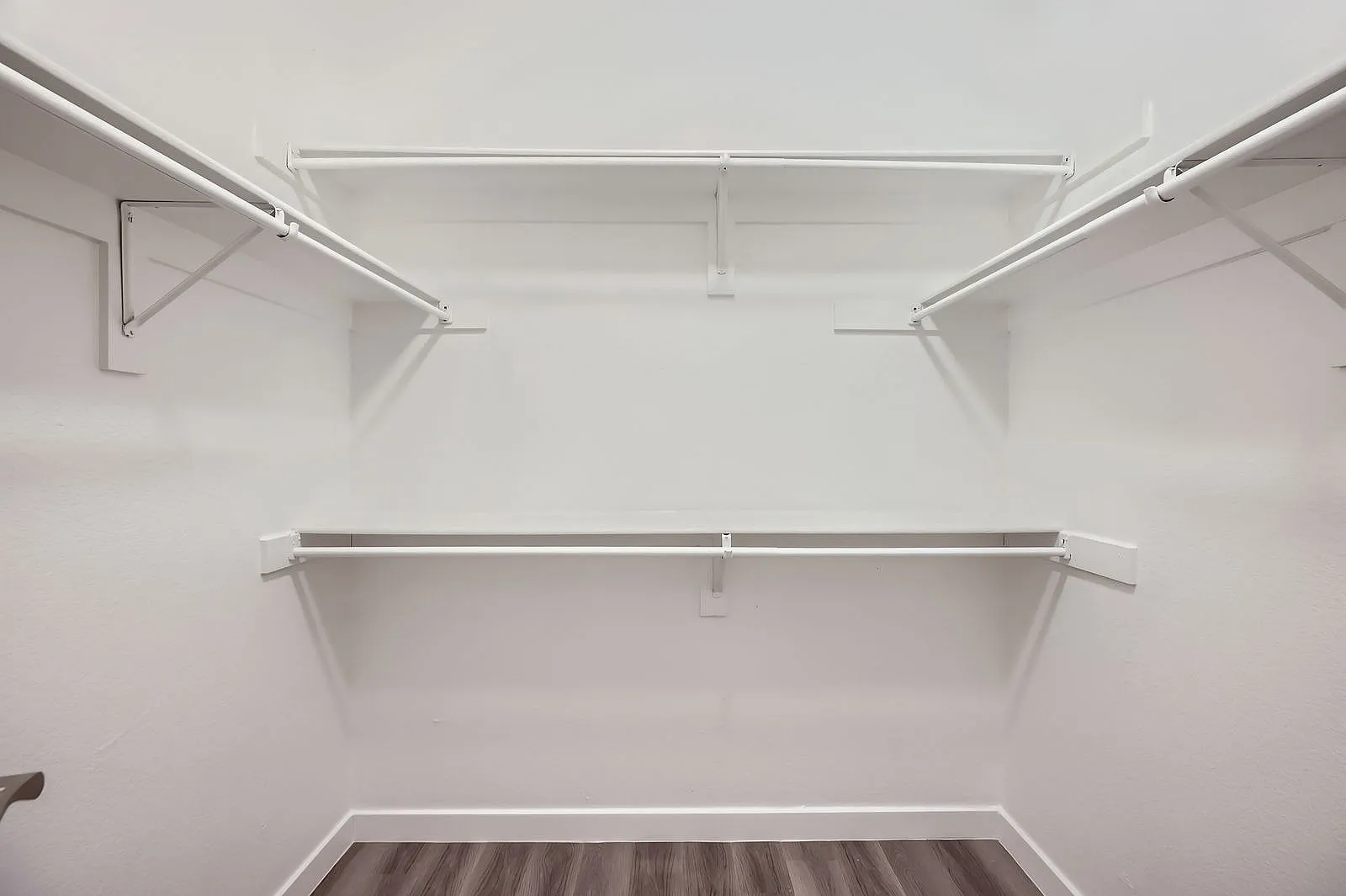 Walk-in closet, chrome hanging rods, white shelving, wood-style plank flooring