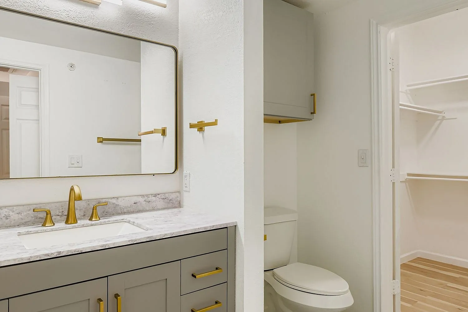 Primary bathroom, gray shaker cabinetry, marble countertops, brass fixtures, rounded mirror