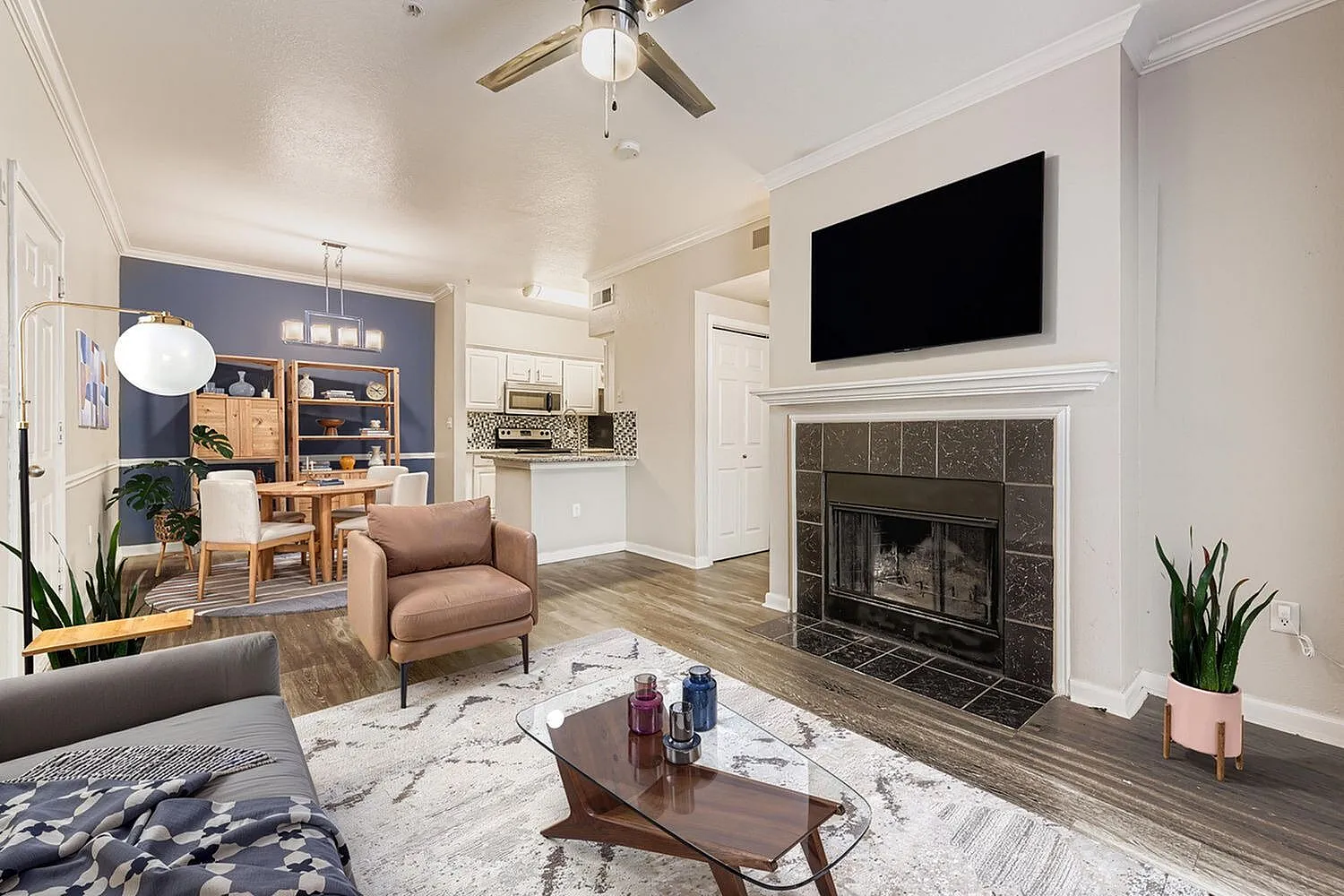 Living room, wood-style plank flooring, fireplace with dark tile surround, wall-mounted TV, ceiling fan