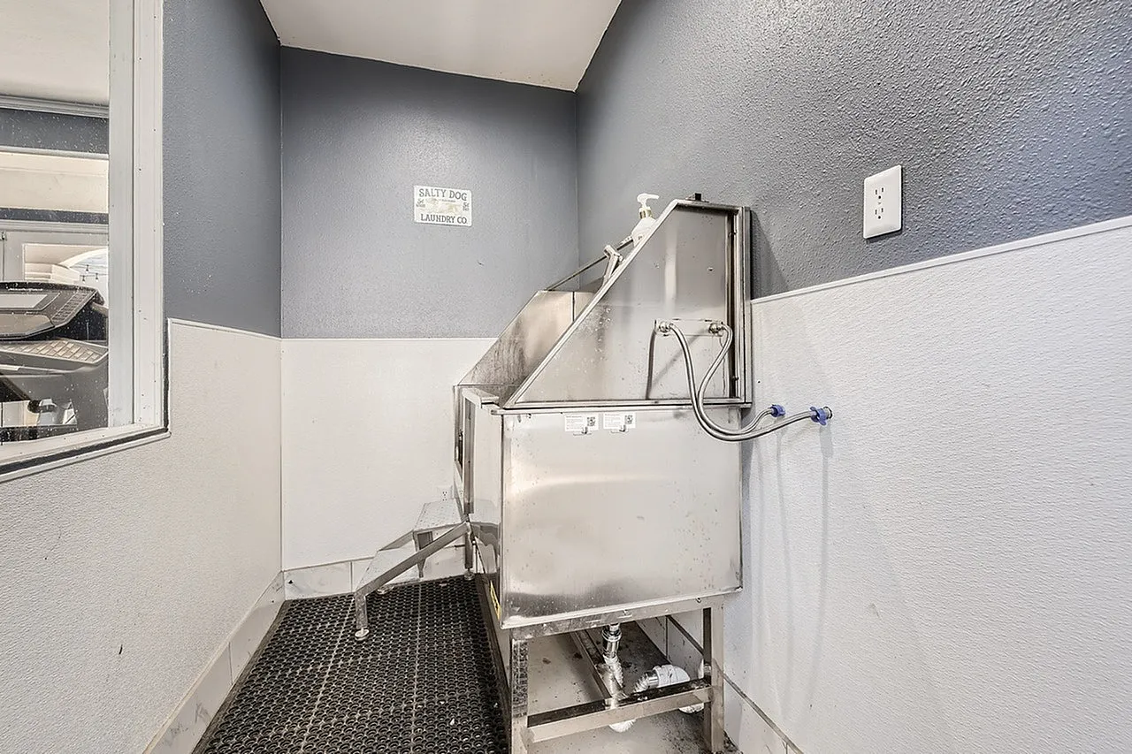 Pet wash station, stainless steel tub, handheld spray, gray and white walls, dark tile flooring