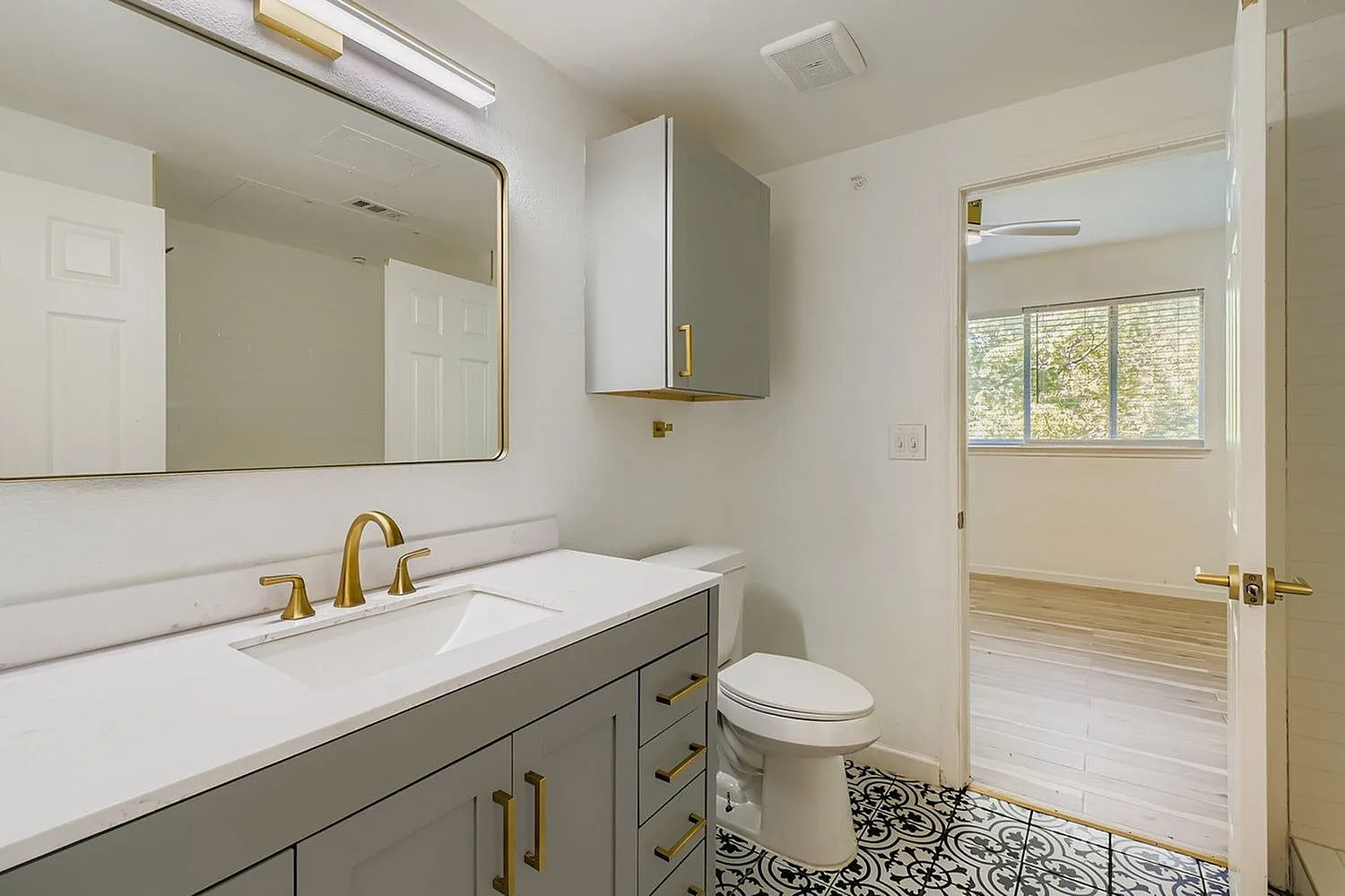 Primary bathroom, gray vanity cabinetry, quartz countertops, brass fixtures, patterned tile flooring