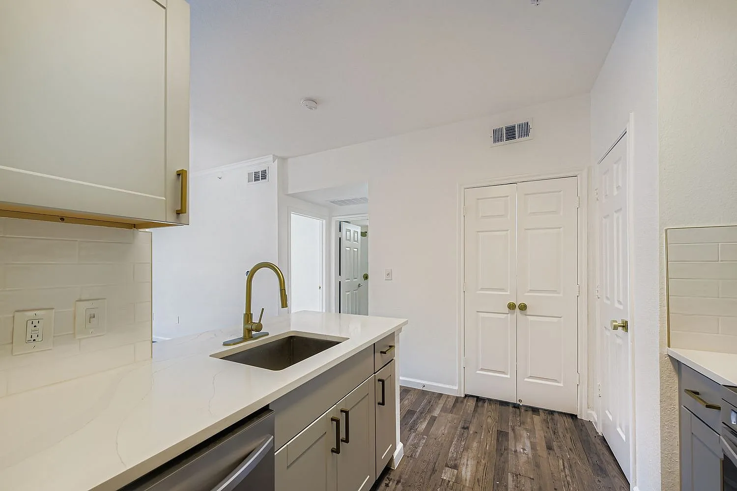 Kitchen with white shaker cabinetry, quartz countertops, bronze faucet, stainless sink, wood-style plank flooring, white subway tile backsplash