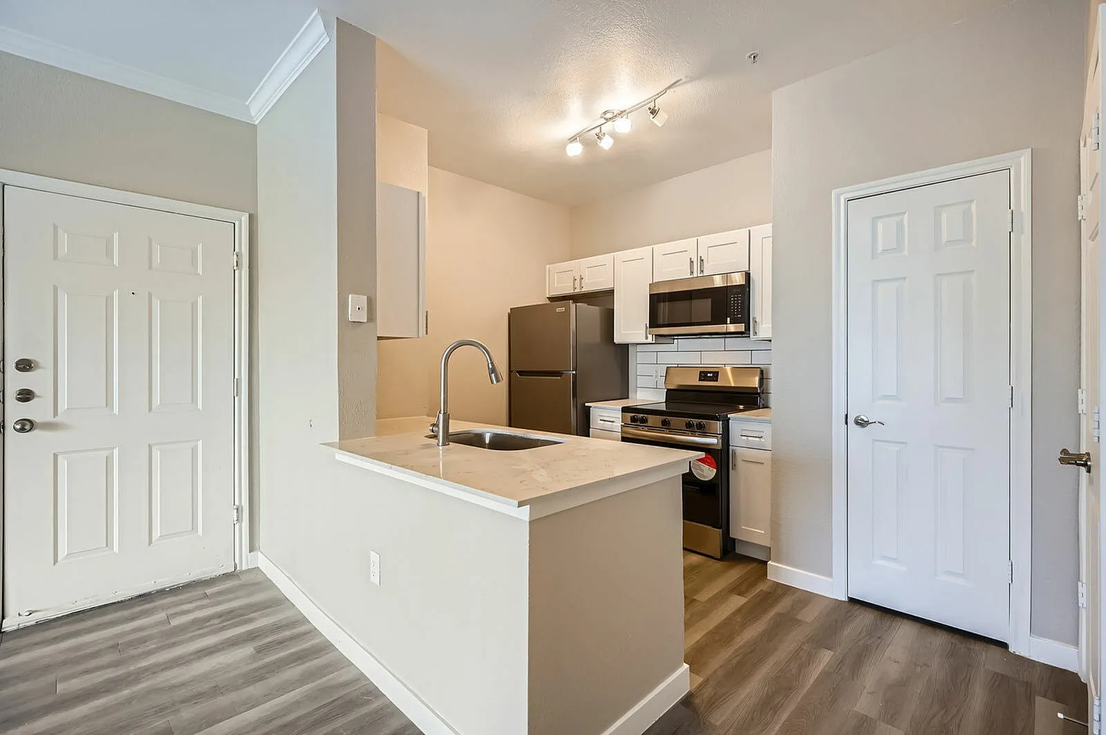 Kitchen, white shaker cabinetry, stainless steel appliances, wood-style plank flooring, entry door