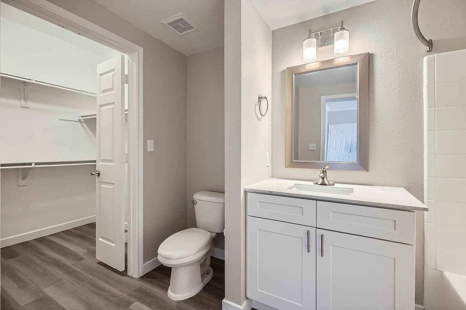 Primary bathroom, white shaker cabinetry, quartz countertop, framed mirror, wood-style plank flooring