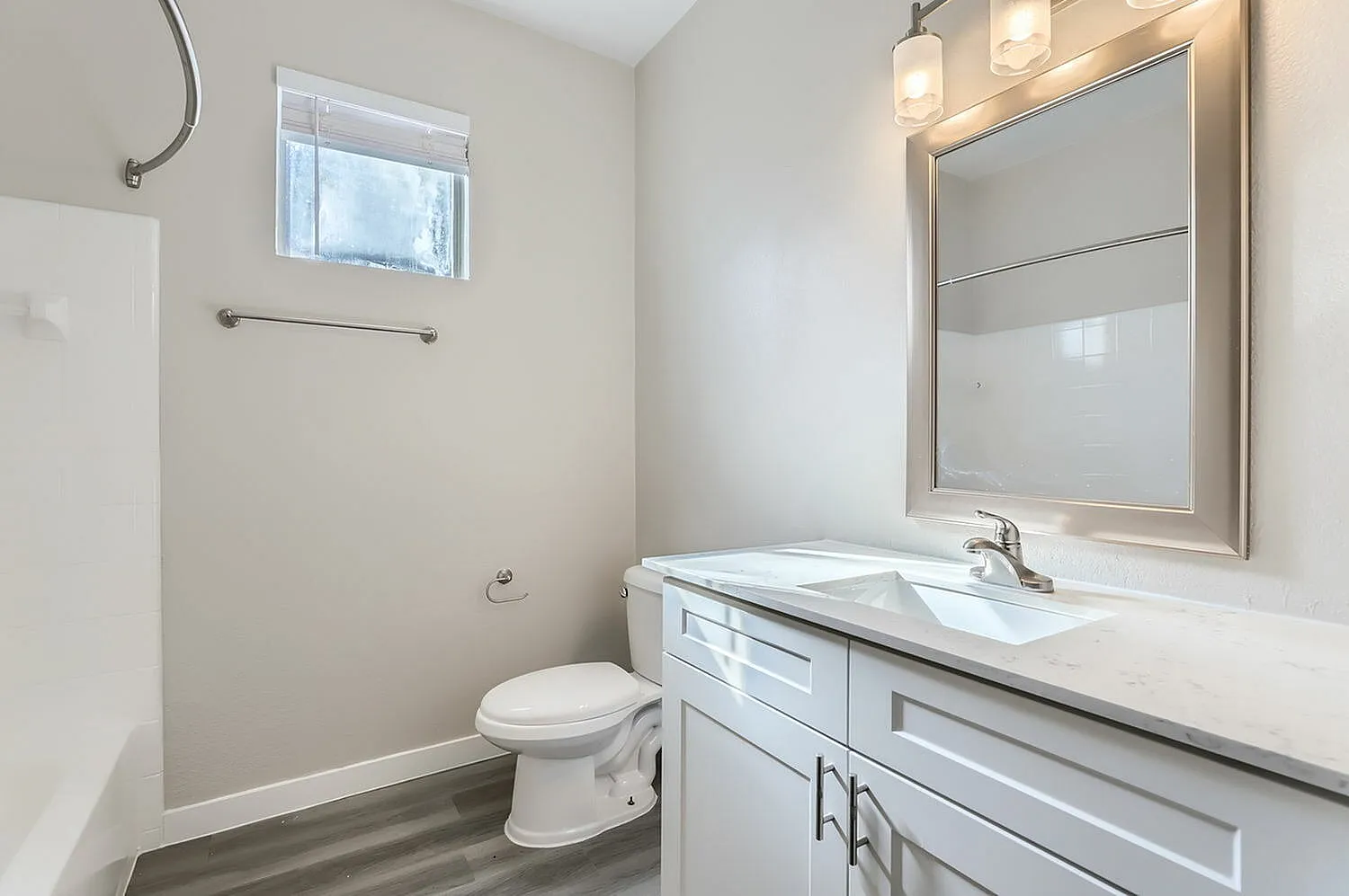 Primary bathroom, white vanity cabinetry, quartz countertops, framed mirror with lighting