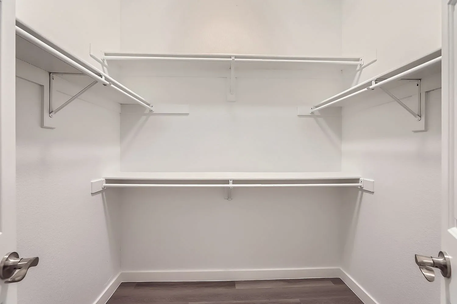 Walk-in closet, metal shelving rods, white walls, wood-style plank flooring