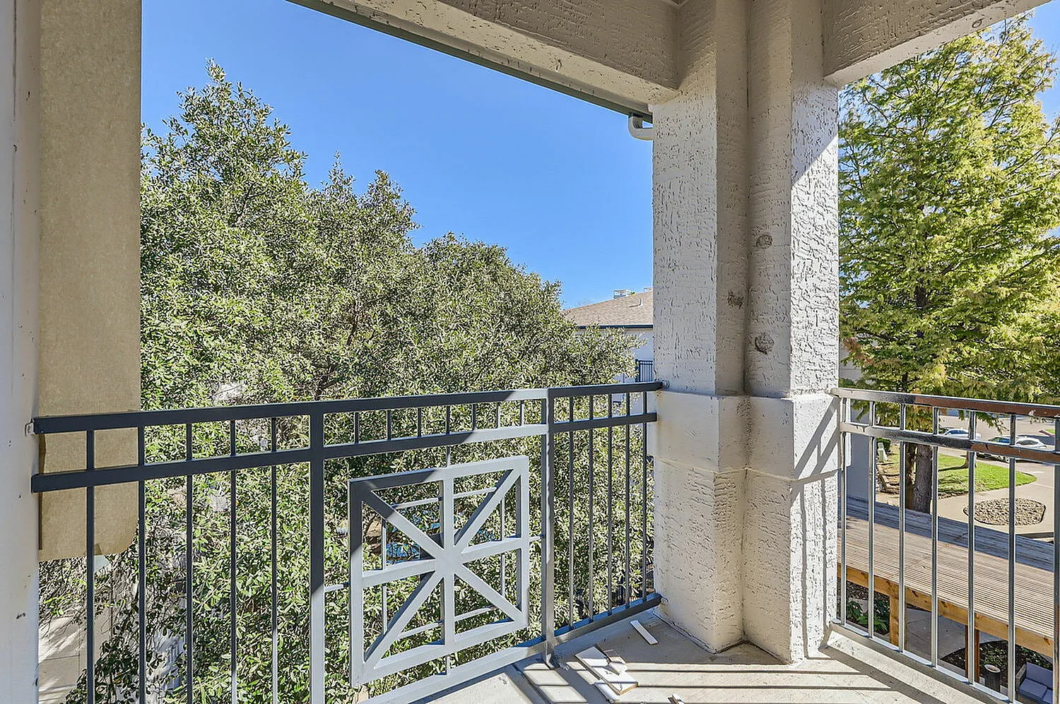 Balcony, metal railing with X-pattern gate, concrete columns, tree views, clear sky
