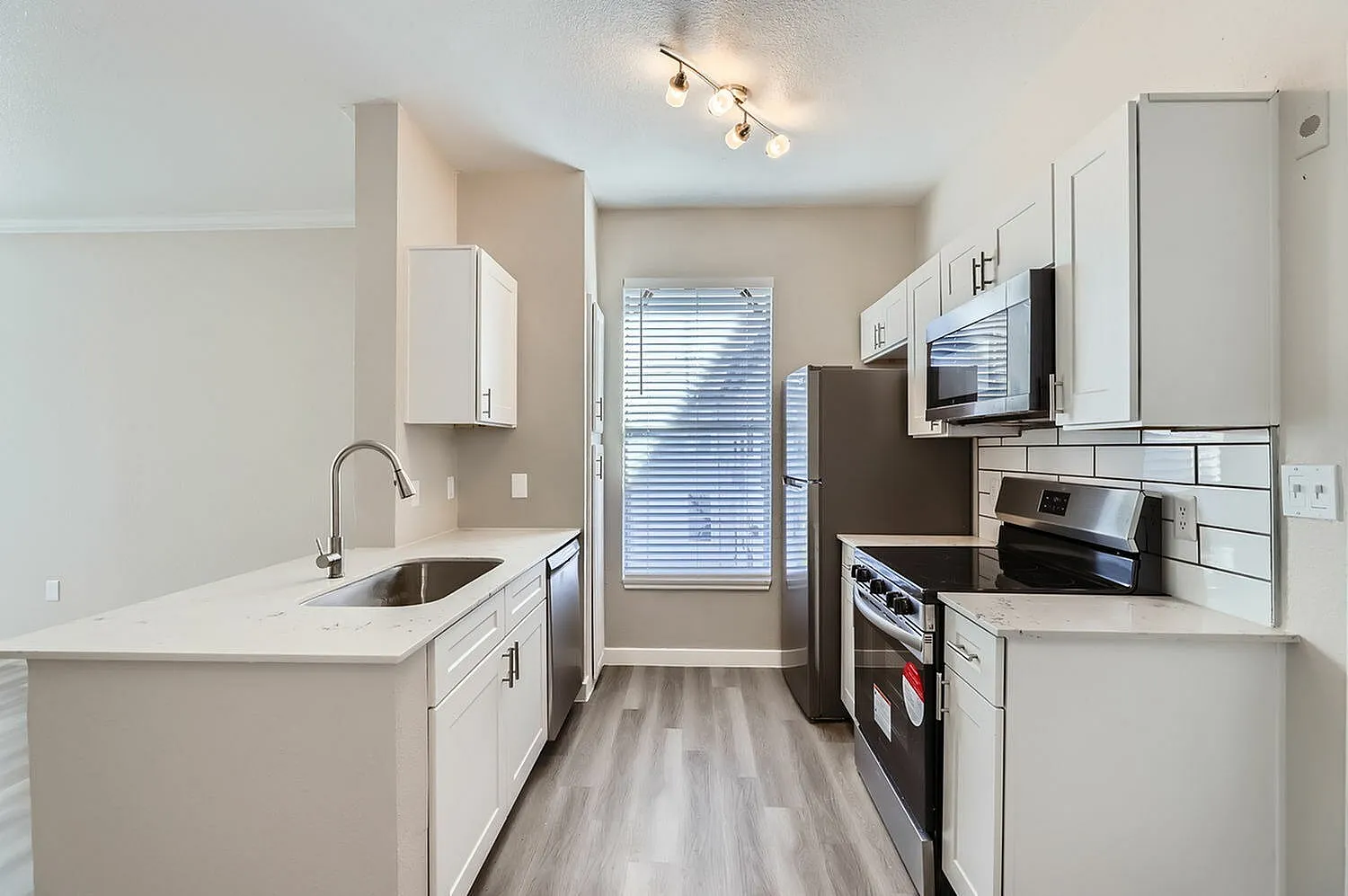 Kitchen, white shaker cabinetry, quartz countertops, stainless appliances, wood-style plank flooring