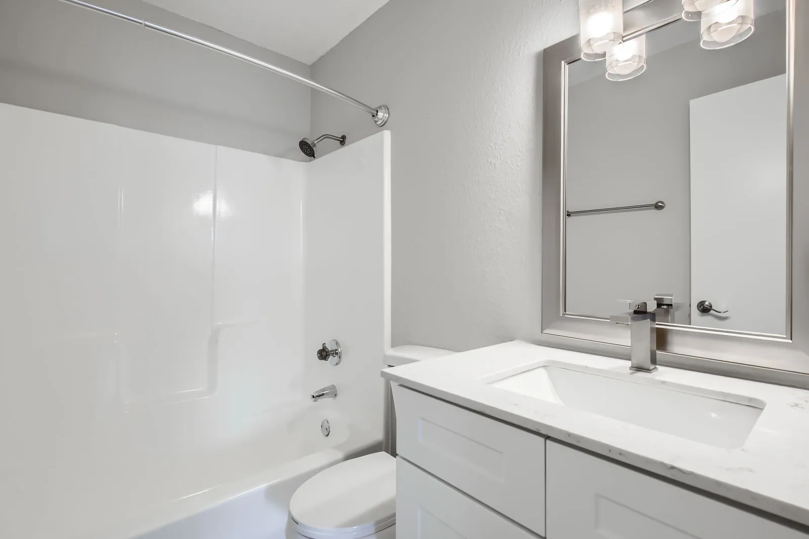 Primary bathroom with quartz vanity countertop, framed mirror, tub-shower combo