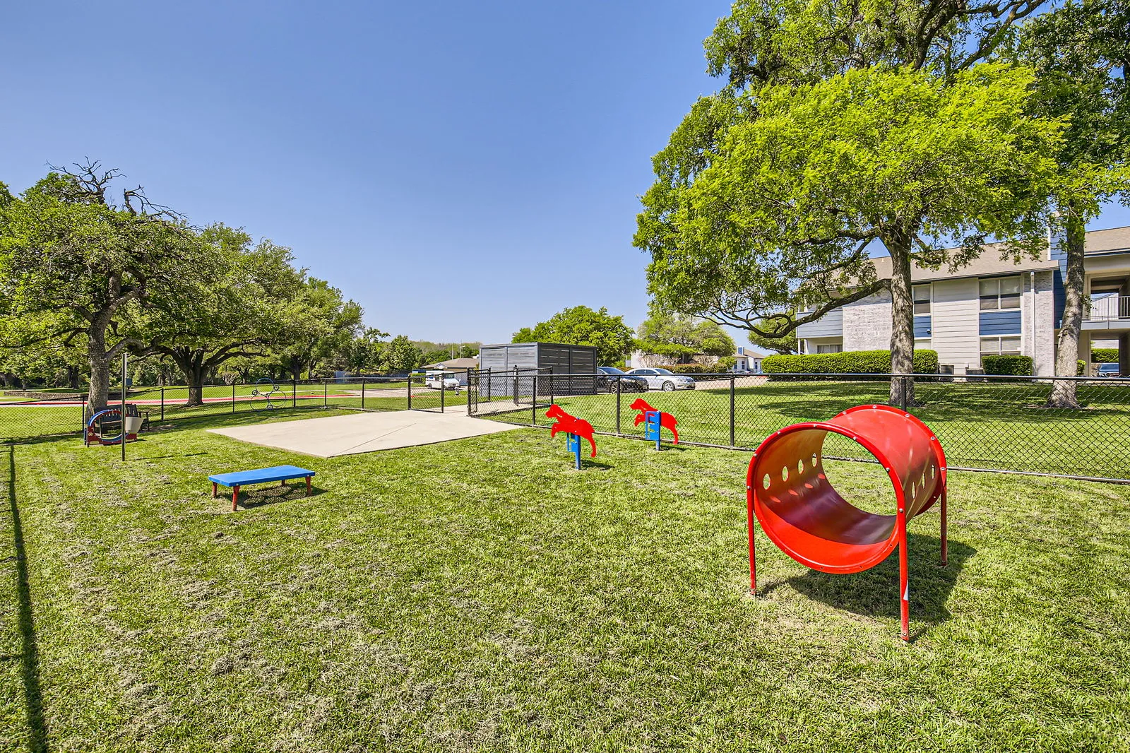 Fenced dog park, agility equipment, open lawn, tree cover