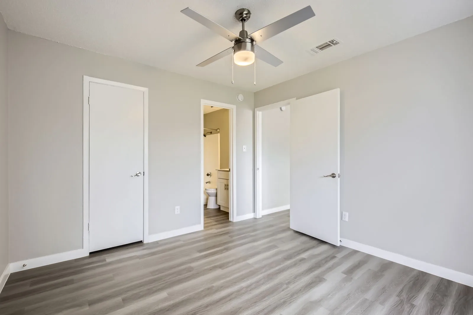 Bedroom with wood-style plank flooring, ceiling fan, closet doors, en-suite bathroom entry