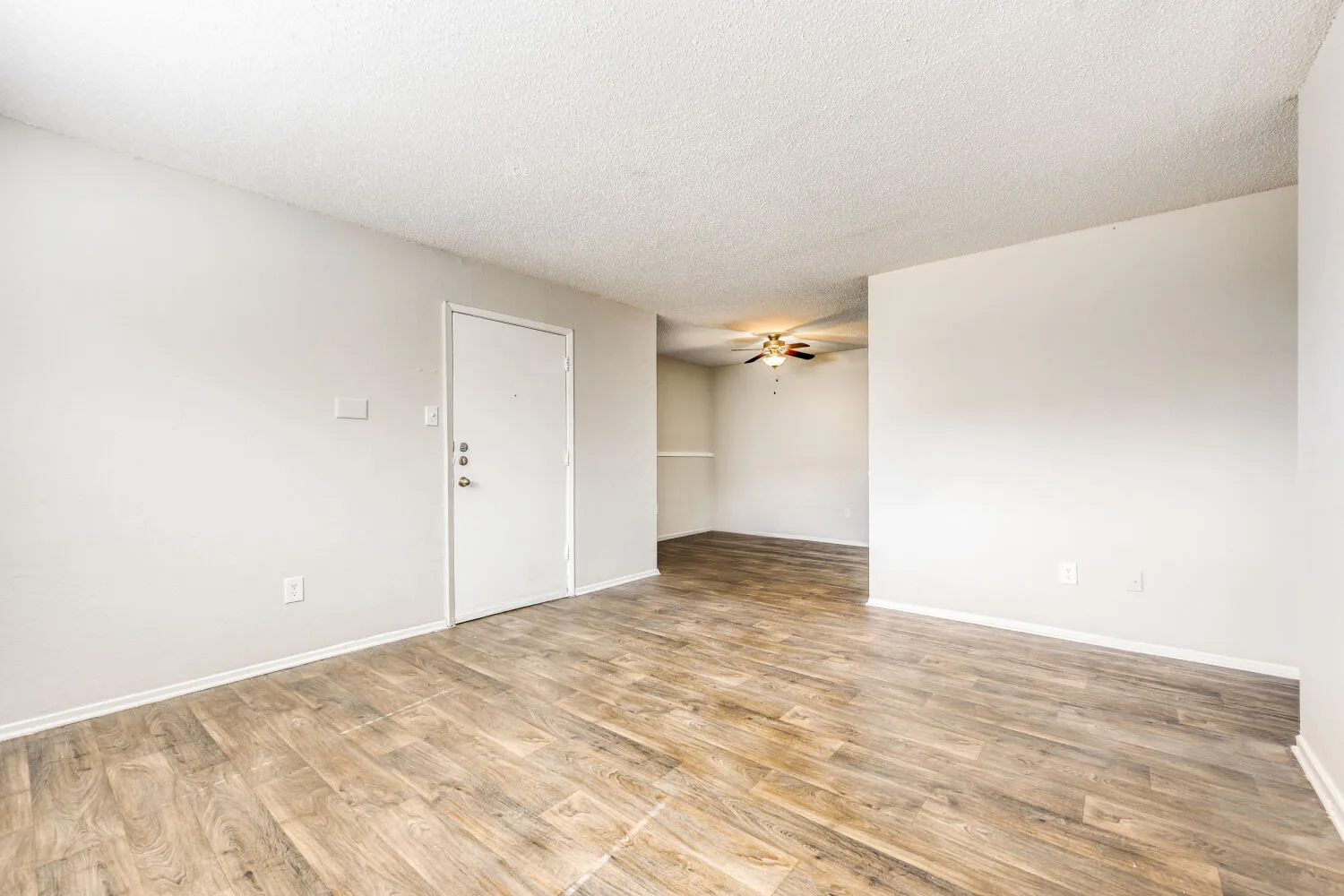Living room with wood-style plank flooring, ceiling fan, entry door, view into dining area