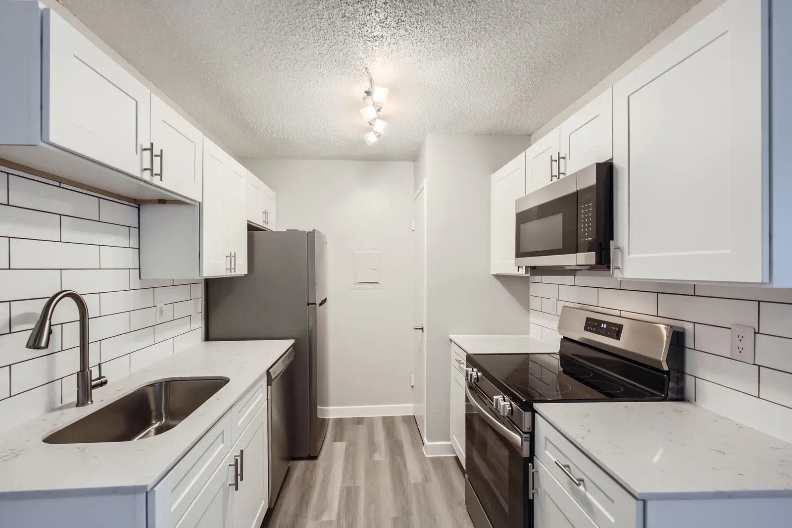 Kitchen with white shaker cabinets, quartz countertops, subway tile backsplash, stainless steel appliances