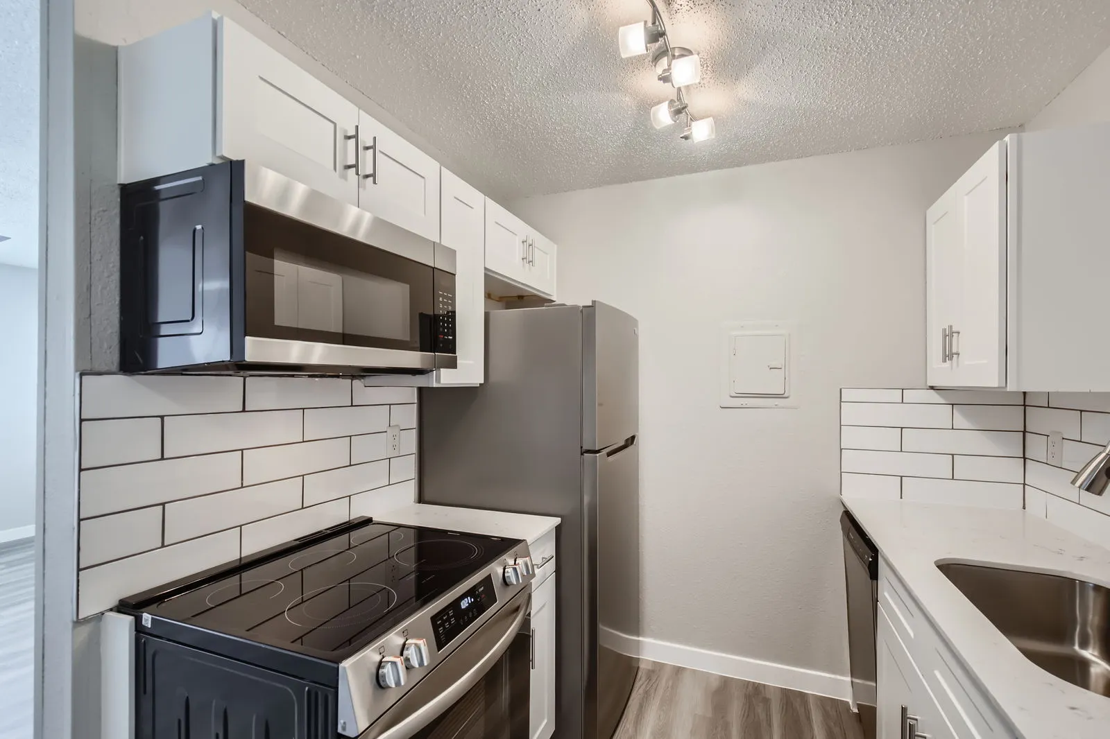 Kitchen with white shaker cabinets, quartz countertops, subway tile backsplash, stainless steel appliances