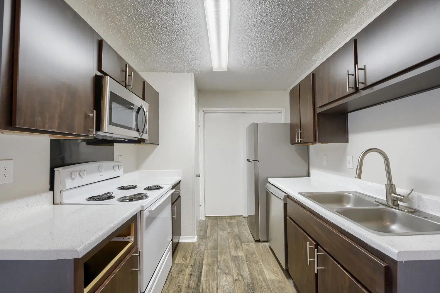 Galley kitchen, dark cabinetry, stainless appliances, wood-style plank flooring