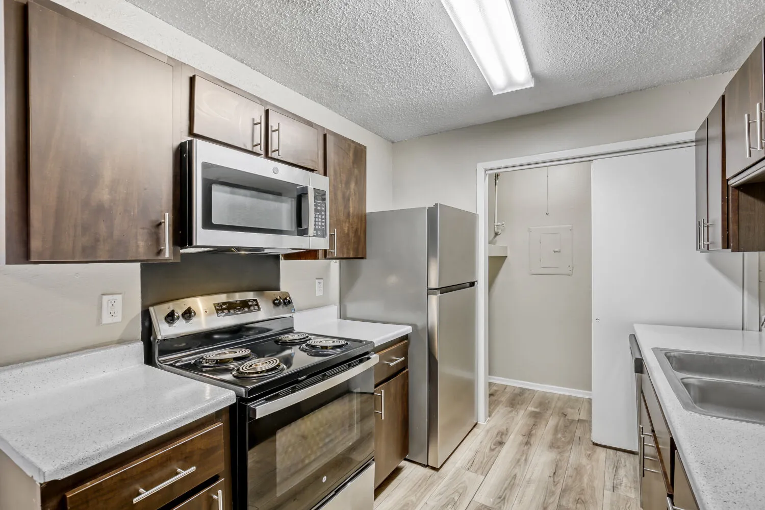 Galley kitchen, dark cabinetry, stainless appliances, wood-style plank flooring