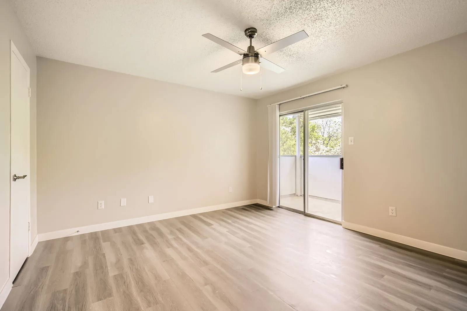 Primary bedroom, wood-style plank flooring, ceiling fan, sliding glass door to balcony