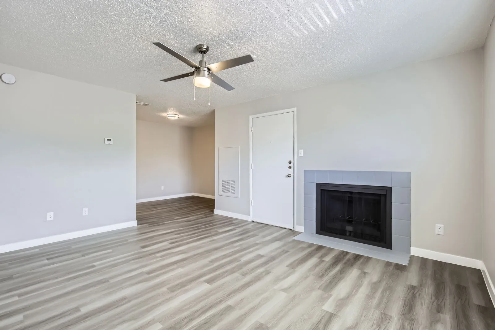 A1 Renovated floor plan, living room with wood-style plank flooring, ceiling fan, fireplace, entry door
