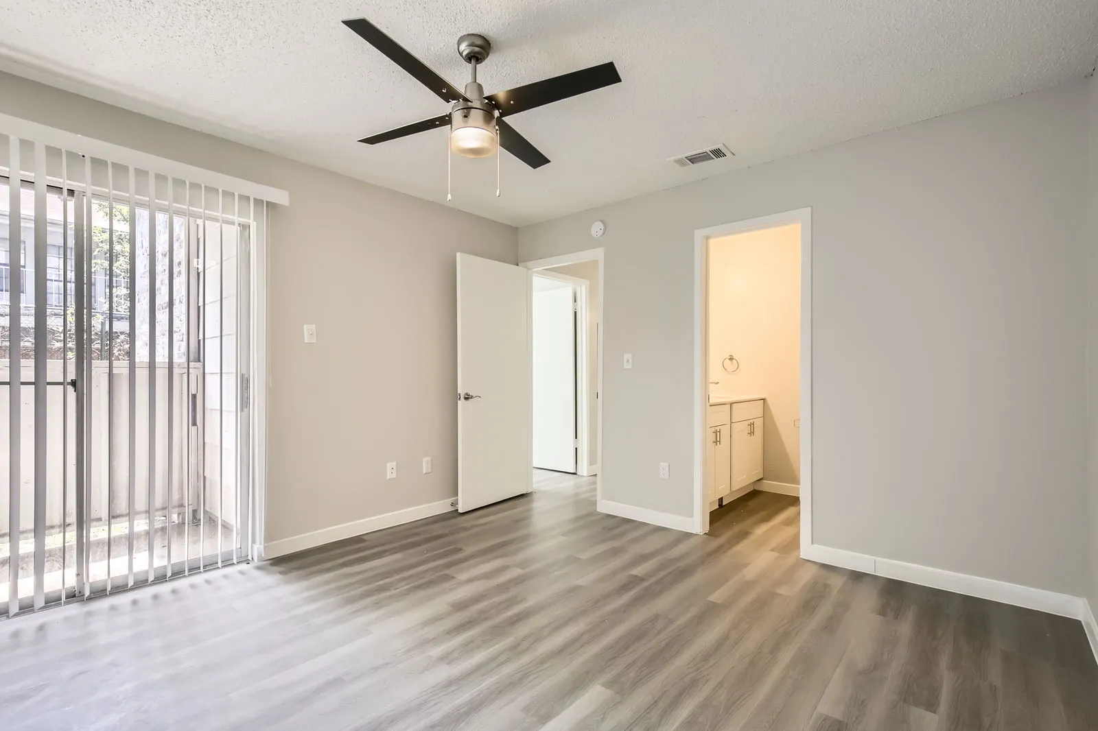 Primary bedroom, wood-style plank flooring, ensuite bathroom access, sliding glass door to patio