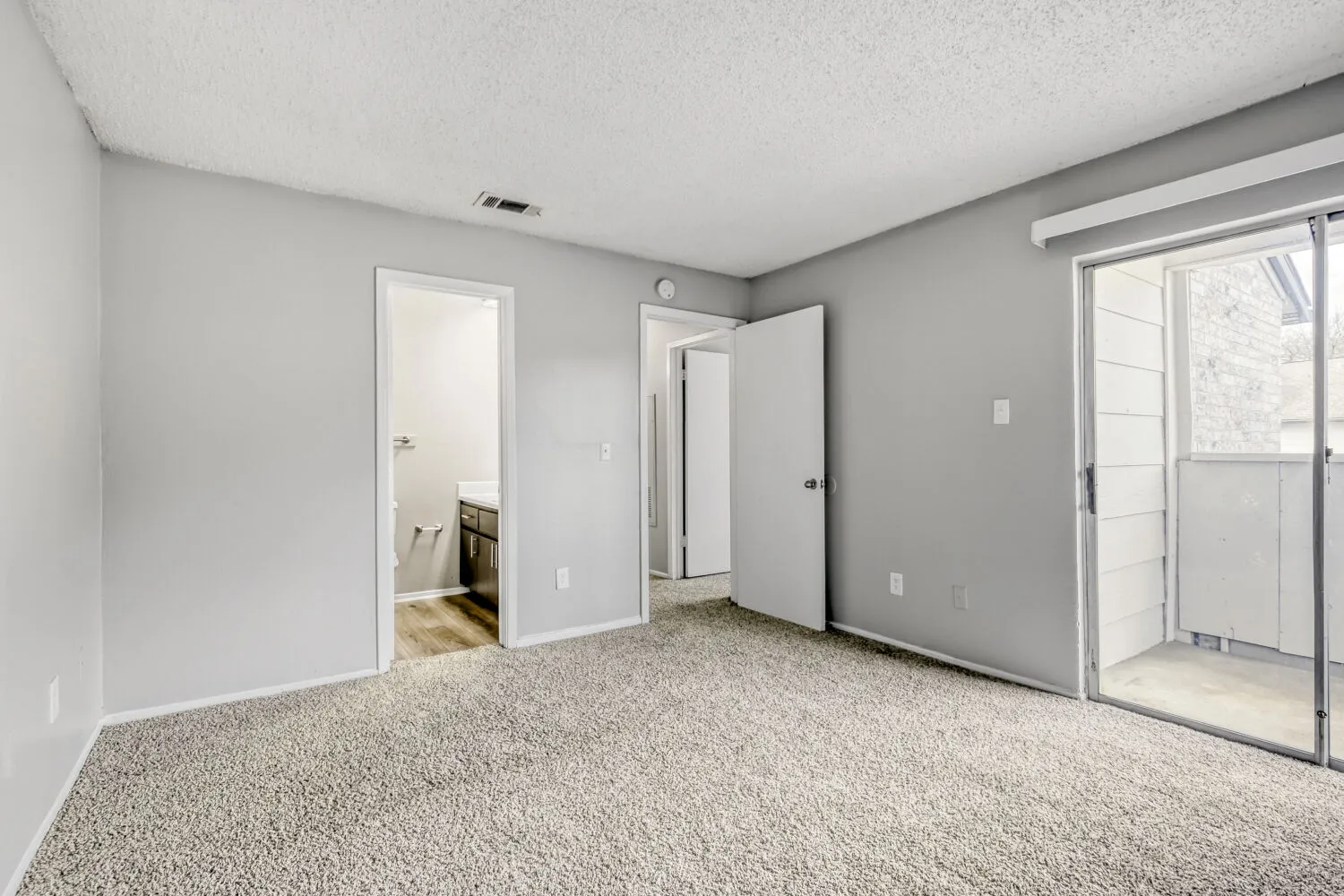 Primary bedroom, carpeted flooring, ensuite bathroom access, sliding glass door to patio