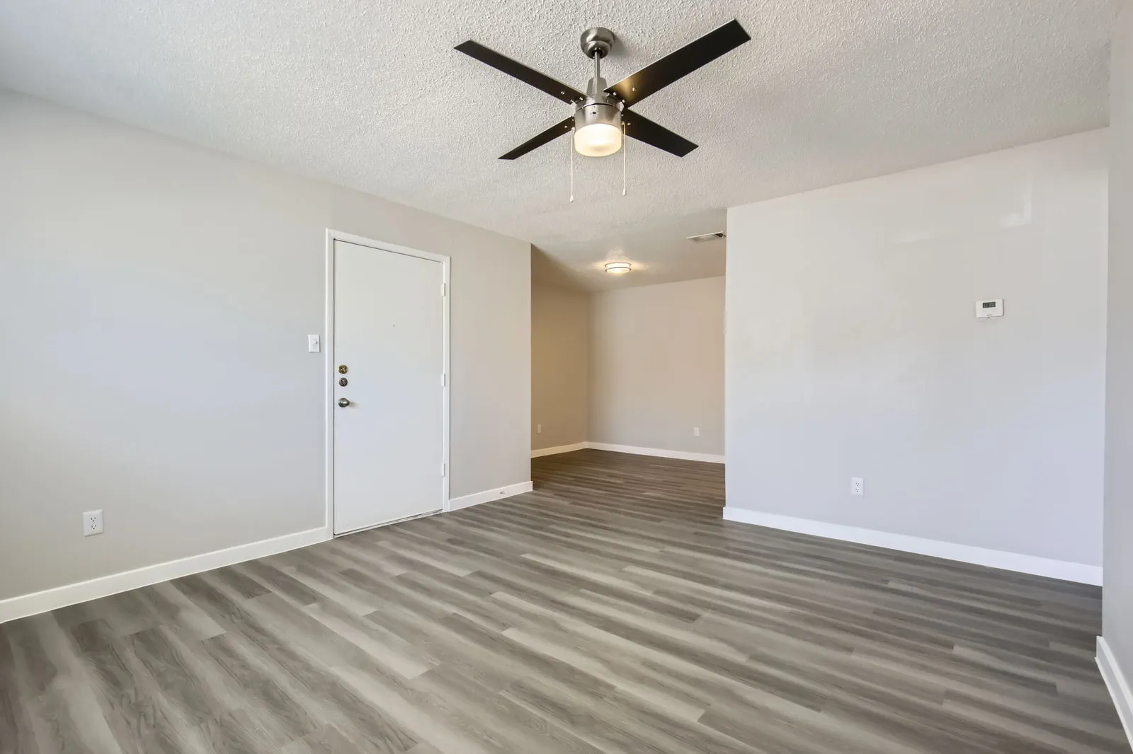 Living room with wood-style plank flooring, ceiling fan, entry door, view into dining area
