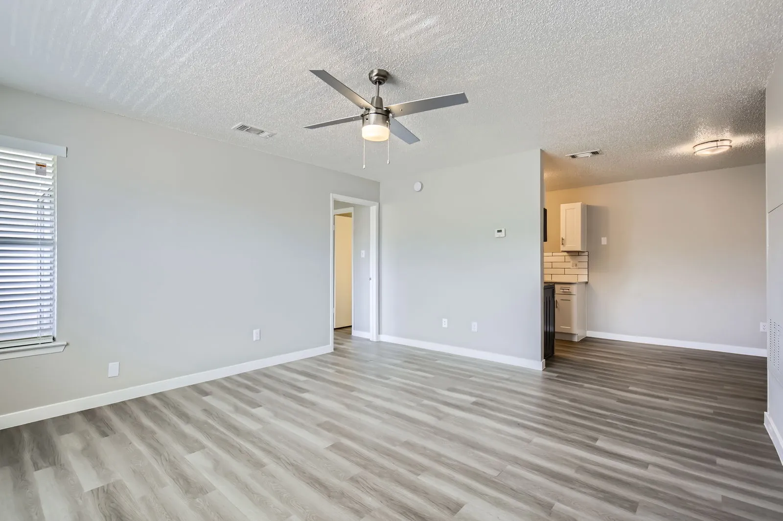 Living room with wood-style plank flooring, ceiling fan, view into kitchen