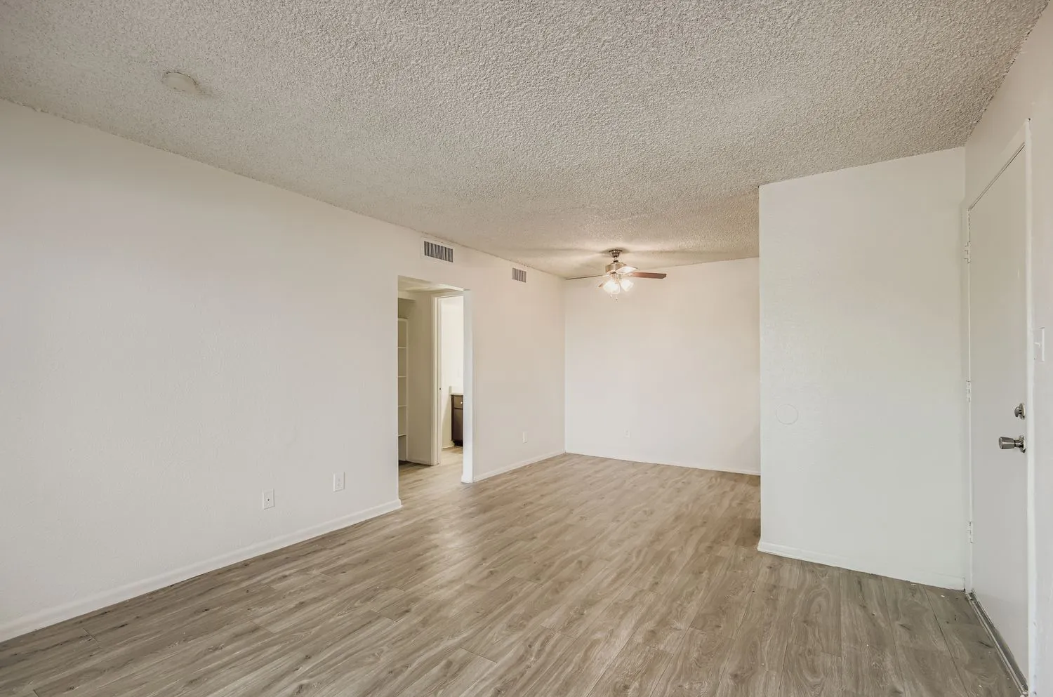 Open living room, ceiling fan, hallway entry, wood-style plank flooring