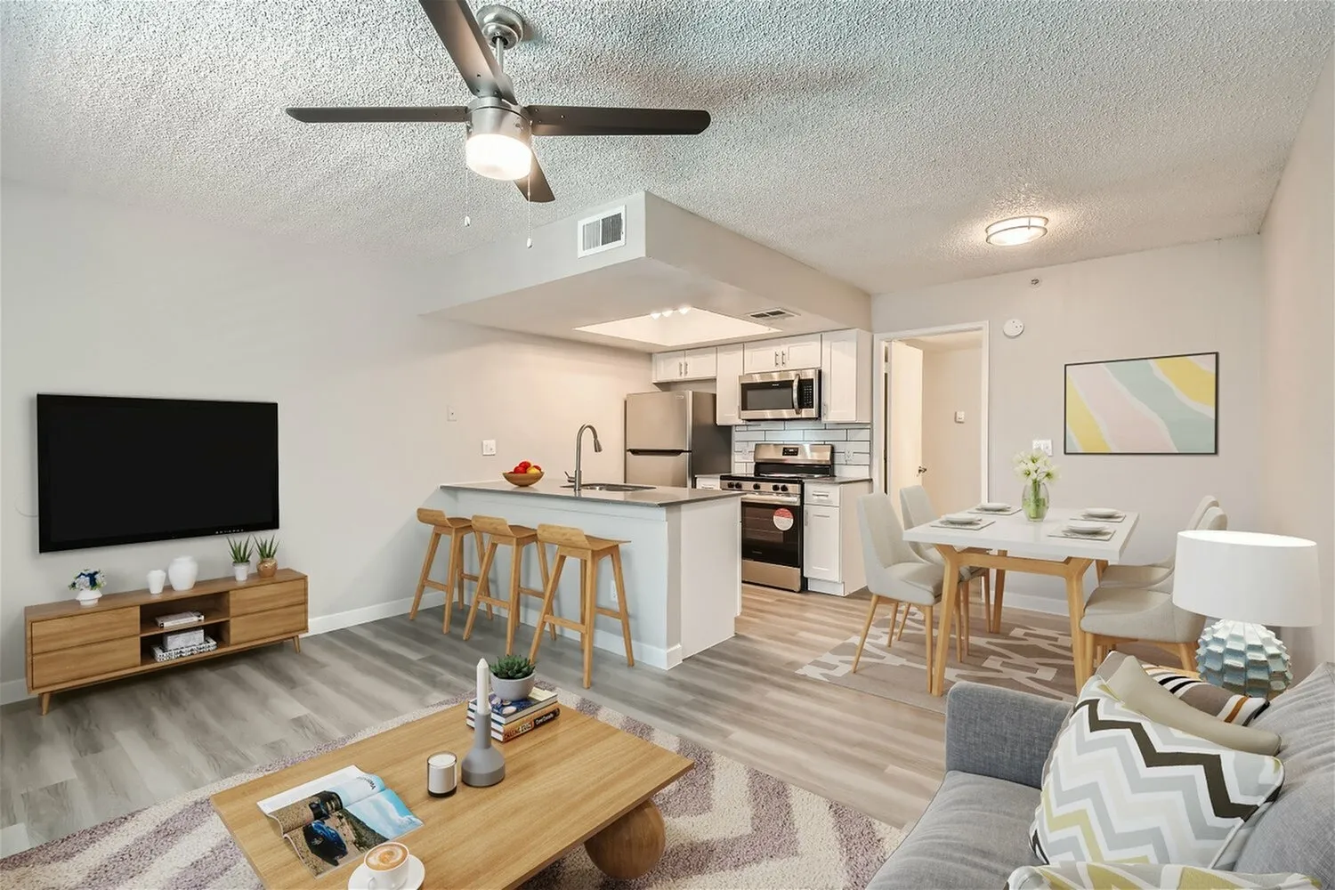 Open concept living and kitchen space, wood-style plank flooring, ceiling fan, stainless steel appliances, wood cabinetry and bar seating