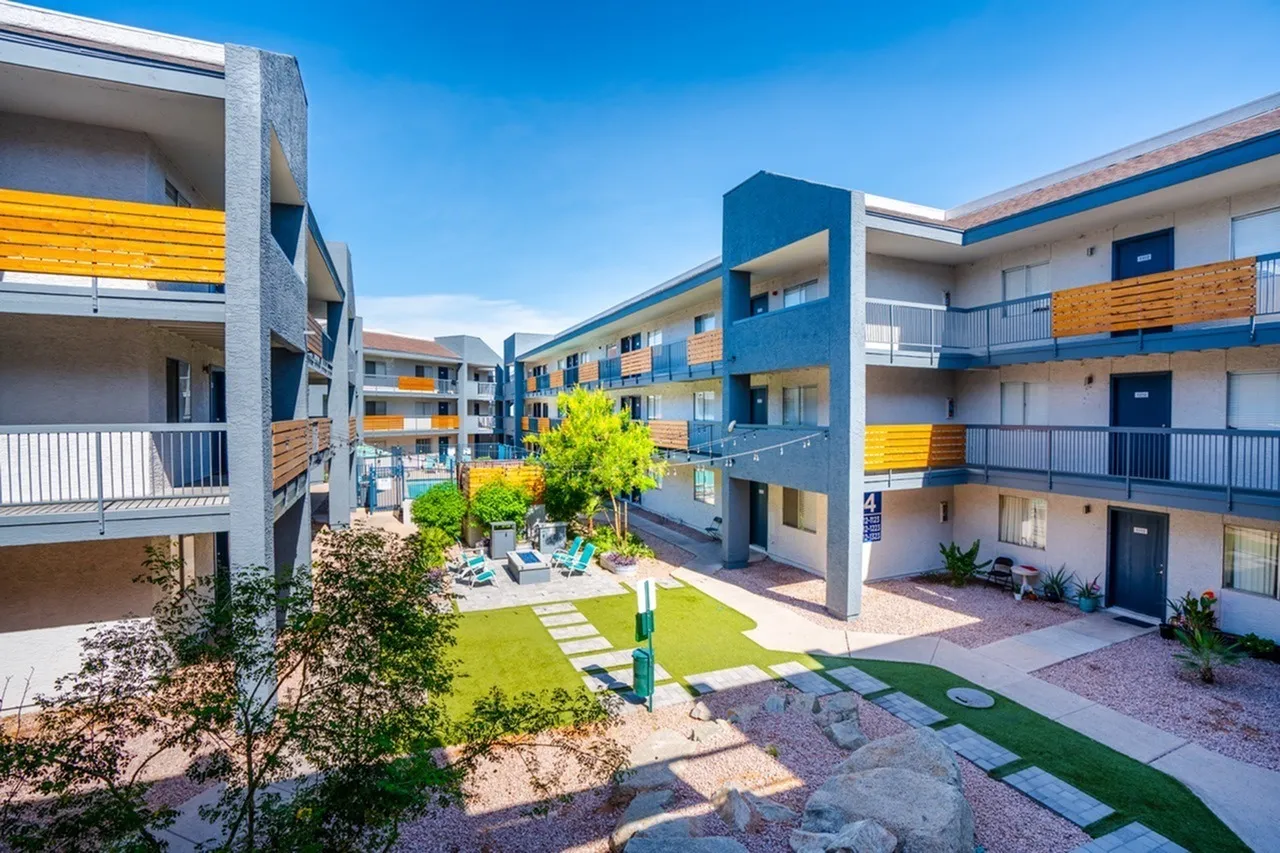 Courtyard with green lawn, stone pathways, central tree, multi-story blue and yellow buildings, clear sky