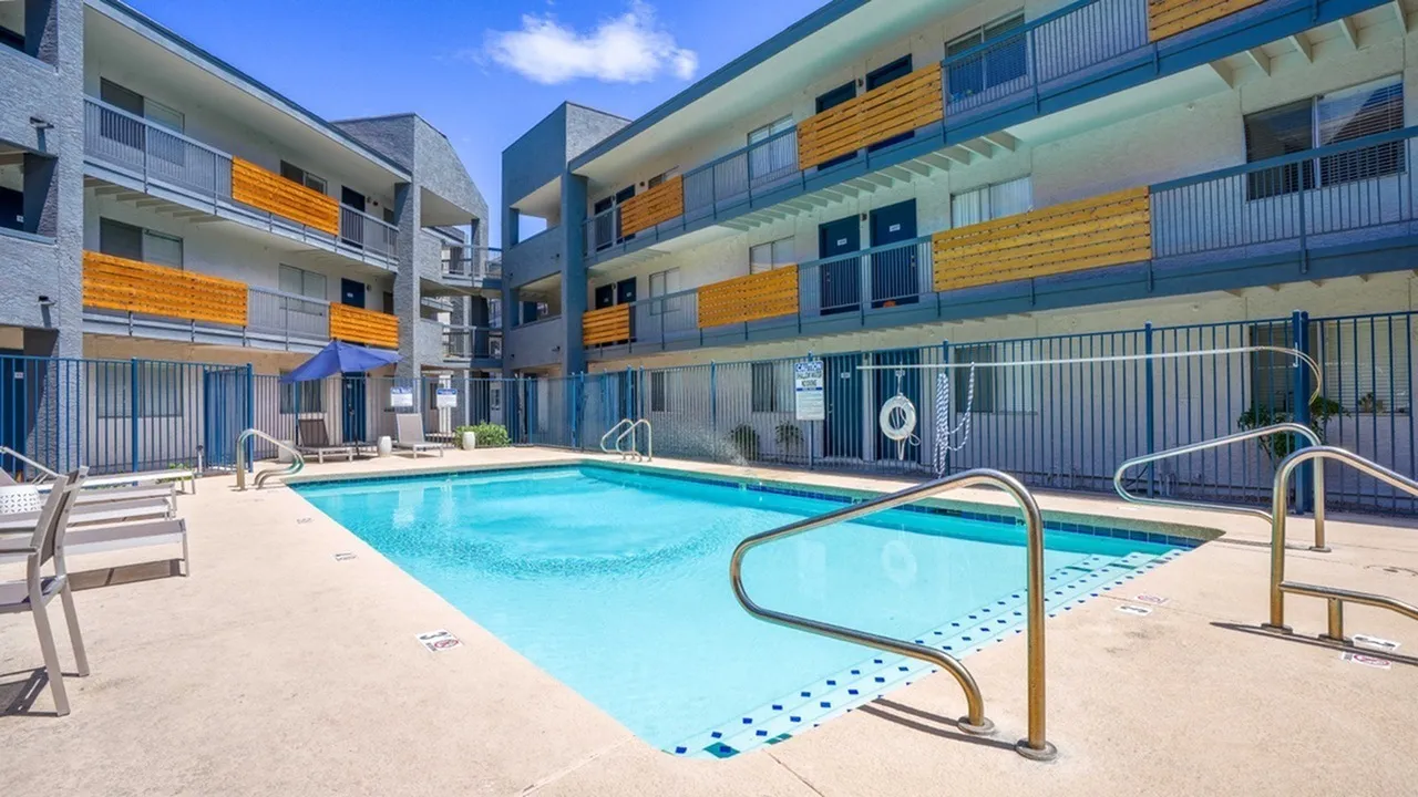Swimming pool, lounge chairs, metal railings, multi-story apartment building