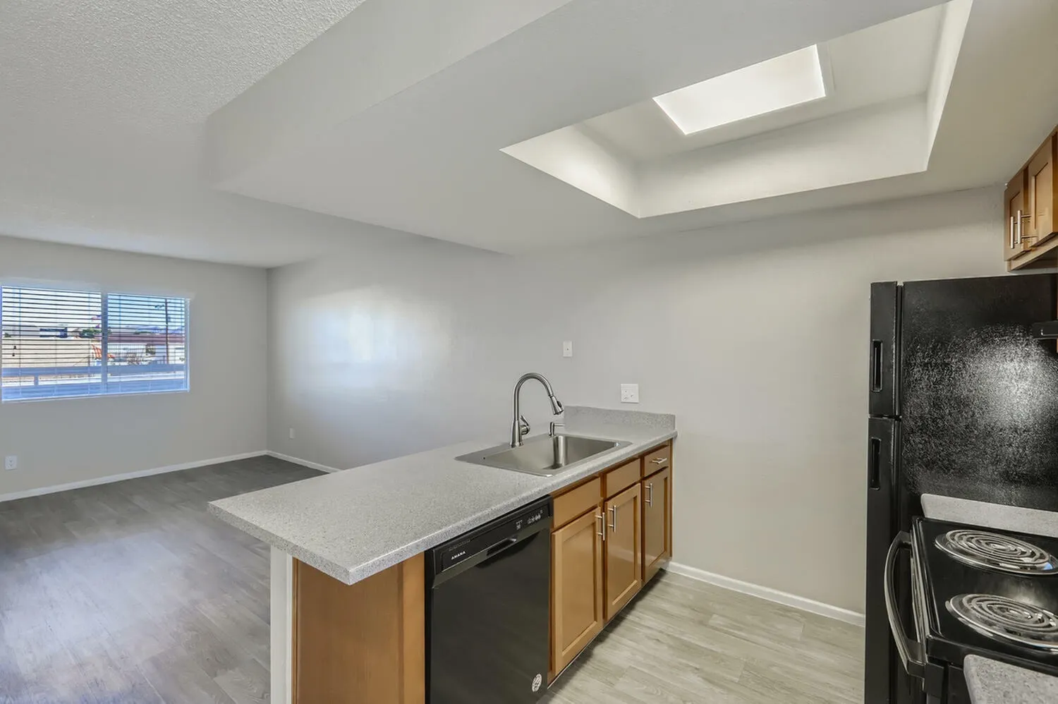 Kitchen, wood cabinetry, white quartz countertops, black appliances, wood-style plank flooring, skylight