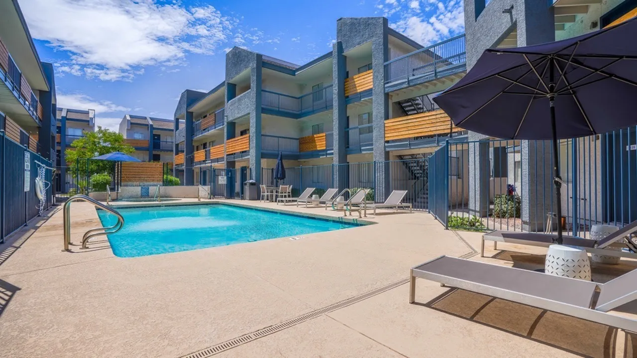 Pool with lounge chairs, umbrellas, modern apartment buildings, clear blue sky